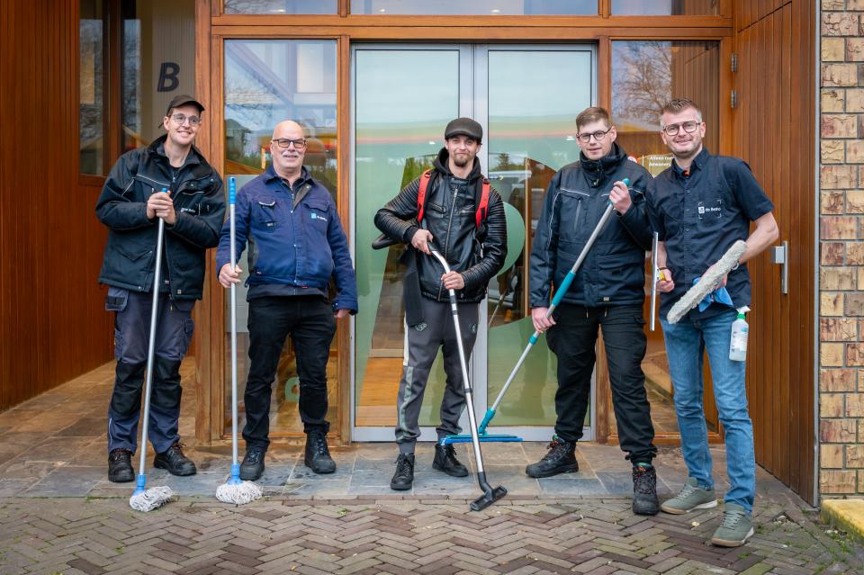 Schoonmaakmedewerkers staan voor de ingang van een gebouw
