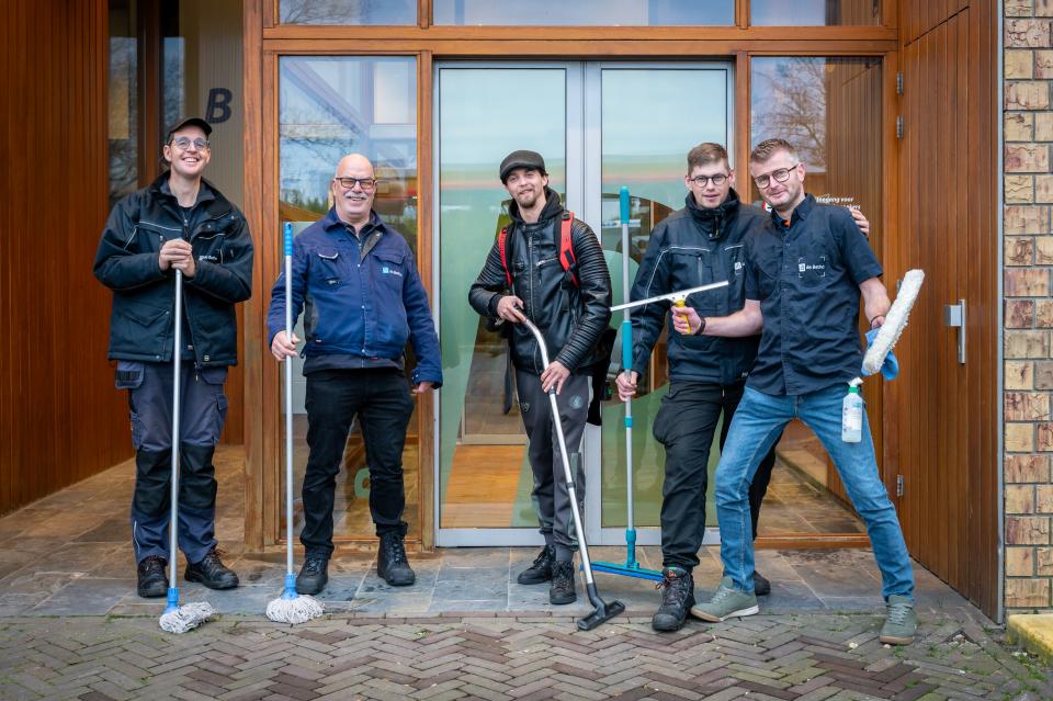Schoonmaakmedewerkers staan voor de ingang van een gebouw
