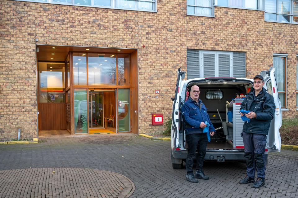 Twee schoonmakers staan bij de achterkant van hun bus